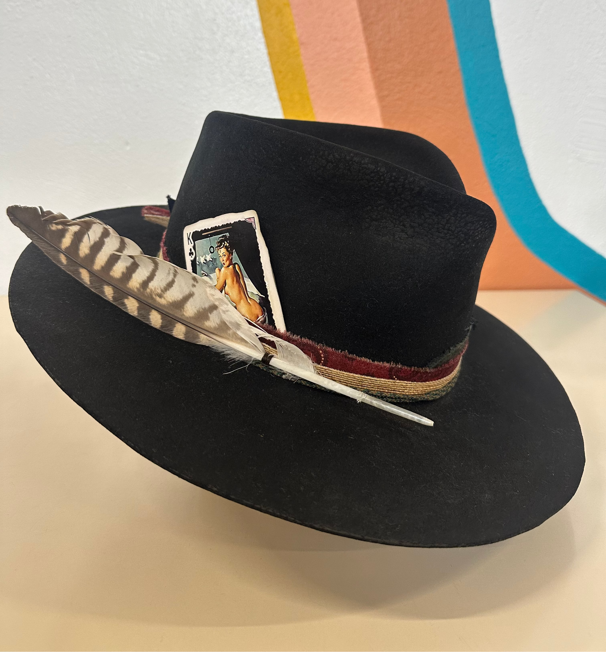 Black hat with a feather and card design on a colorful background